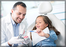 dentist teaching a baby girl how to brush her teeth